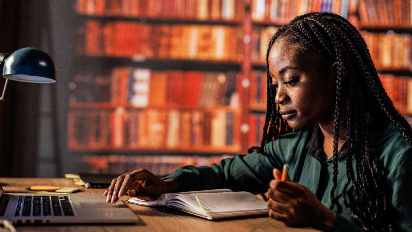 African-America student looking at book and touching laptop