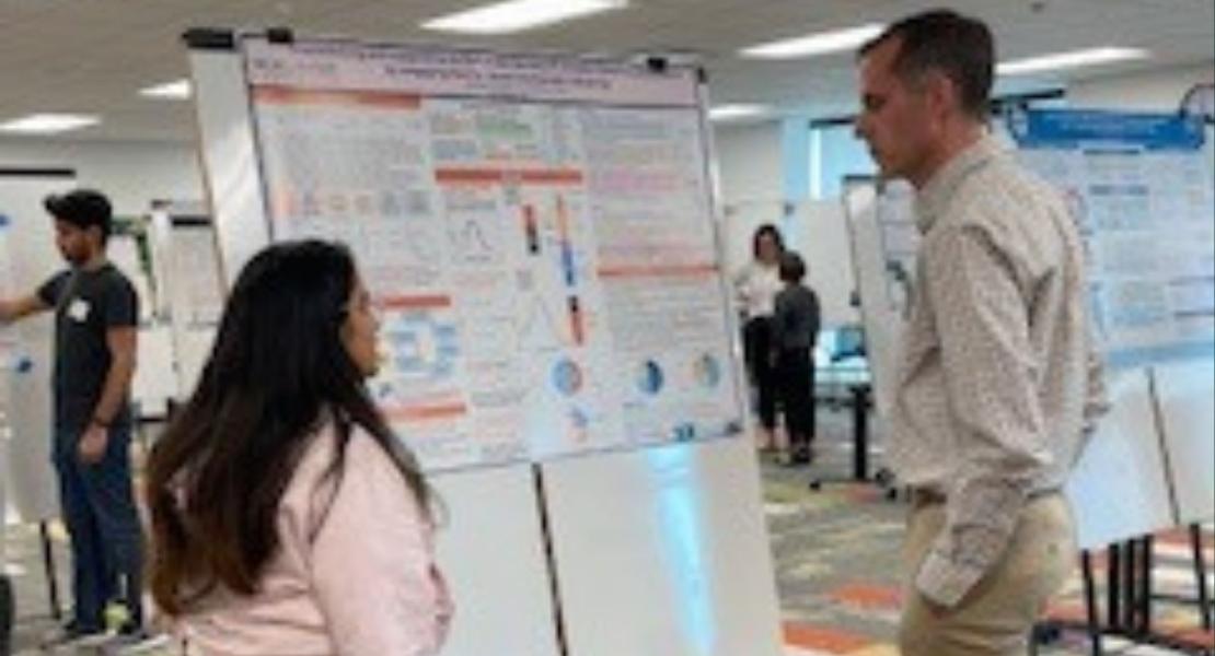 Poster presenter in front of poster speaking to onlooker