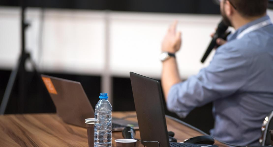 Male adult student with laptop in front of him speaking into microphone