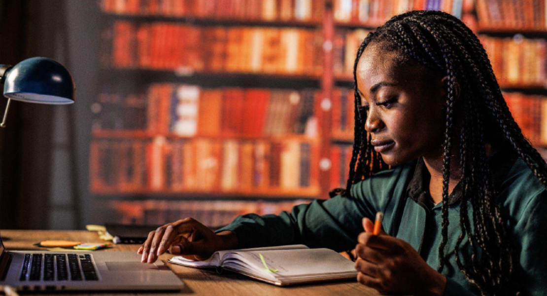 African-America student looking at book and touching laptop