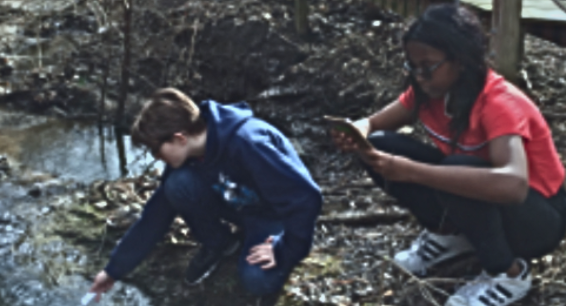 White male student and African-American female student kneeling by river 